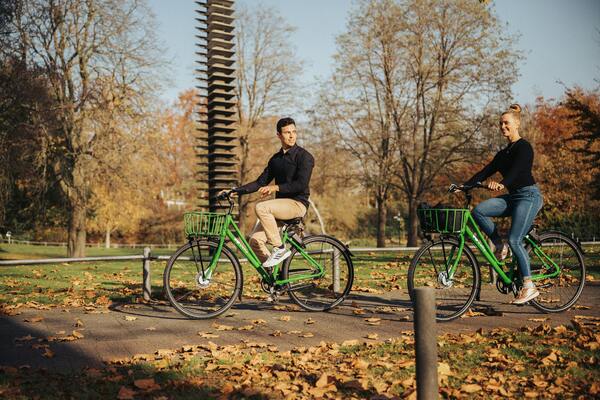 A man and a woman cycling together in a park.