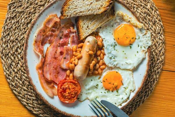 English breakfast with sausages, egg, bacon, tomato, baked beans and bread.