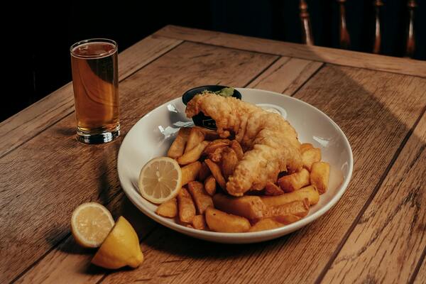 Bowl of fish and chips with a drink and sliced lemon on the side