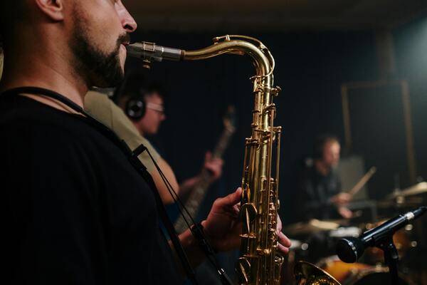 Man playing a Saxophone with a band in the back playing other instuments