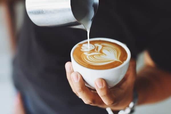 A barista pouring milk on coffee