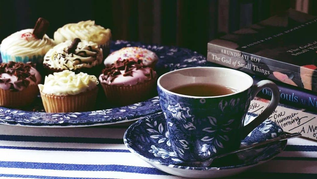 plate of cupcakes with a mug of tea and books on the side